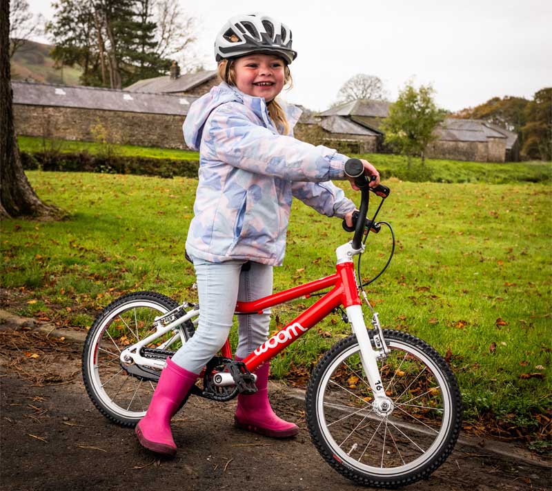 A little girl stands (smiling) astride a woom brand bike